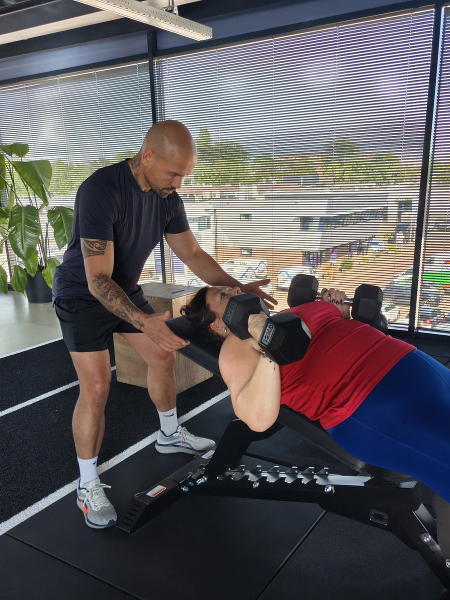 Personal trainer spot een klant tijdens een dumbbell bench press bij Fit Up Leiderdorp
